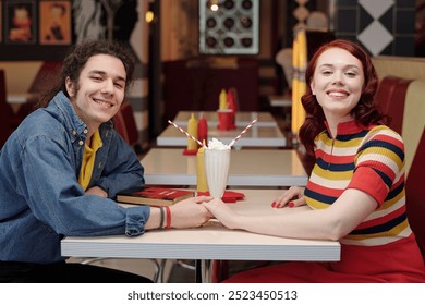 Young couple happily sitting at a retro diner table while holding hands and enjoying milkshakes place has a nostalgic ambiance - Powered by Shutterstock