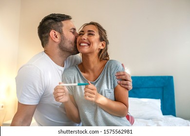 Young couple is happy because of positive pregnancy test. Affectionate couple finding out results of a pregnancy test in their bedroom. Family, parenting and medical concept