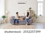 Young couple, happy family with dog on sofa switching on air conditioner, blowing warm, cold air room temperature control for optimal home environment, providing ideal climate control heating system