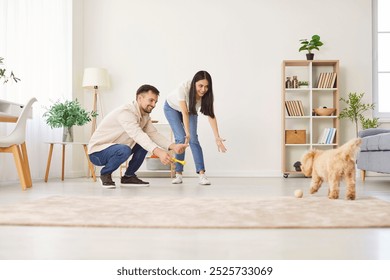 Young couple, happy family playing with cute pet puppy at home, childfree spouses enjoy time together having fun with small pedigreed dog on carpet, indoor leisure activity in new modern living room - Powered by Shutterstock