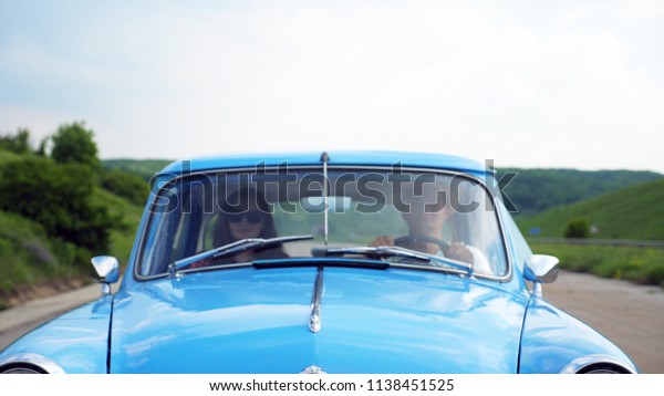 Young couple in hats riding in vintage car at\
summer travel. Man and woman sitting at the front seat of old retro\
car during ride. Concept of road trip at holidays . Slow motion\
Close up Front view.
