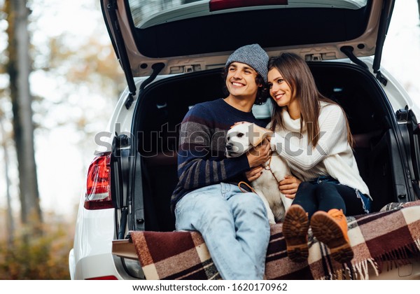 Young couple have a weekend\
time with their labrador retriver sitting in car in the autumn\
forest.