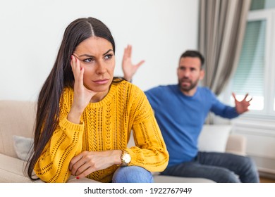 Young couple having an argument while sitting on their couch at home. Tired frustrated wife ignoring angry husband arguing blaming upset woman of problems, jealous man shouting at sad girlfriend