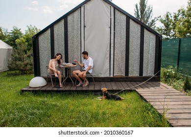 Young Couple Having Breakfast In The Backyard With A Dog