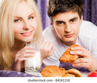 Young Couple Having Breakfast In Bed - Man Eating Croissant, Female With Milk Moustache