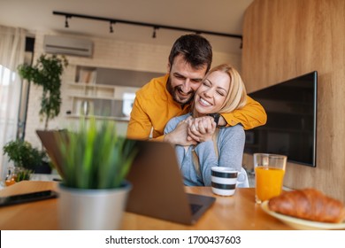 Young couple having breakfast at home. Happy couple using laptop and having breakfast together. - Powered by Shutterstock