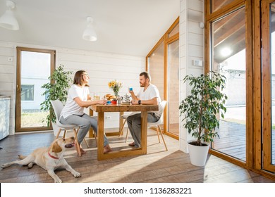 Young couple having a breakfast sitting with dog in the dining room in the wooden country house - Powered by Shutterstock