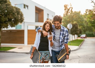 Young couple having fun carrying long boards and looking at the mobile phone in the city. - Powered by Shutterstock