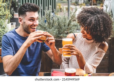 Young Couple Having Fun At Restaurant, Two Diverse Friends Eating Burgers At Fast Food And Drinking Beer