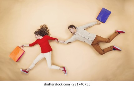 Young Couple Having Fun Running With Shopping Bags Against The Beige Background