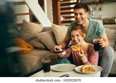 Young couple having fun while eating pizza and watching TV in the living room.  - Powered by Shutterstock