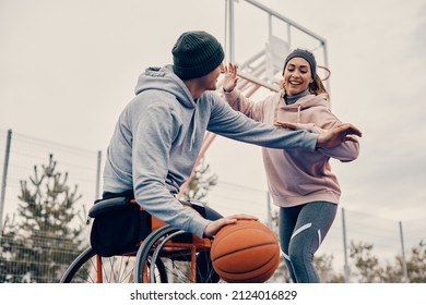 Young couple having fun while playing basketball on outdoors sports court. Man is using wheelchair. 