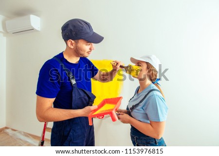 Young couple having fun while painting wall at home in yellow with paintbrush and paint stick roller. Young couple having fun while renovating and moving in concept.