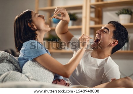 Young couple having fun while feeding each other with biscuits in the bedroom. 