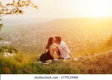 Young couple having a picnic at the hill. Man is  kissing his girlfriend. Sunset over mountain in the background. Romance, dating and love concept. Romantic love story. - Powered by Shutterstock