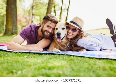 Young couple having picnic with their dog in the park, lying on blanket and looking at camera - Powered by Shutterstock