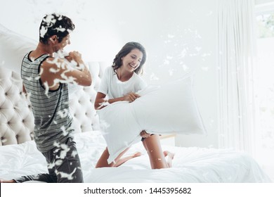 Young Couple Having A Pillow Fight In Their Bedroom. Man And Woman Fighting With Pillows On Bed.