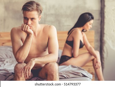 Young couple having a problem. Handsome man is leaning on his hand while sitting sadly on bed, woman is sitting in the background