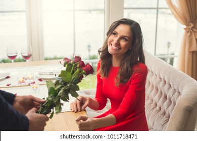 Young Couple Having Romantic Dinner In The Restaurant Giving Flowers