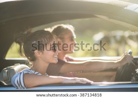 Young couple in his car, happy to drive on a country road, focus on the woman. There are some blurred cows at the background