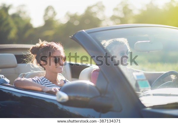 Young couple in his\
convertible car, happy to drive on a country road, focus on the\
woman. Shot with flare