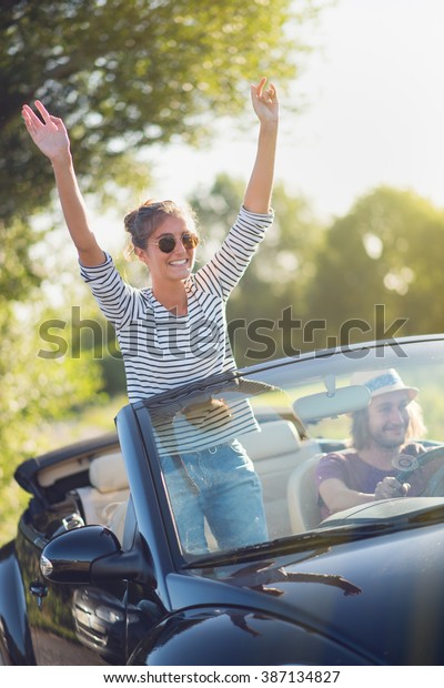 Young couple in his convertible\
car, happy to drive on a country road in summer.Shot with\
flare