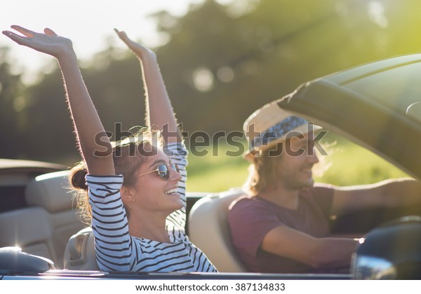 Young couple in his\
convertible car, happy to drive on a country road, focus on the\
woman. Shot with flare