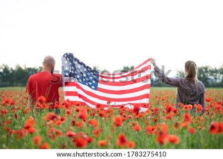 Young couple holding Flag of the United States in beautiful summer field on a clear, sunny day. Celebrating Independence Day, National holiday concept.