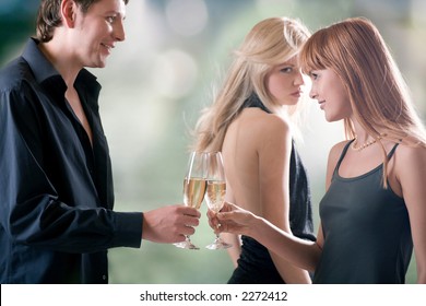 Young couple holding glasses with champagne and woman looking for them, outdoors, focus on woman with red hair and man