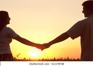 Young couple holding hands and looking at each other on sunny summer day.