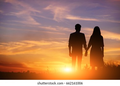 young couple is holding hands on a background sunset silhouette.