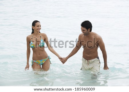 Young couple holding hands and walking in ocean (high angle view)