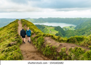 A young couple holding hands while walking towards the Grota do Inferno viewpoint at Sete Cidades on Sao Miguel Island, Azores. The adults are walking away from the camera and looking at the lake view