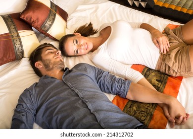 A young couple holding hands while lying on the bed in a asian style hotel room.