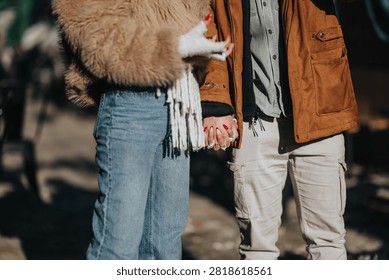 A young couple holding hands while standing together in casual winter clothes. The pair share a quiet moment outdoors, dressed in jackets and jeans.