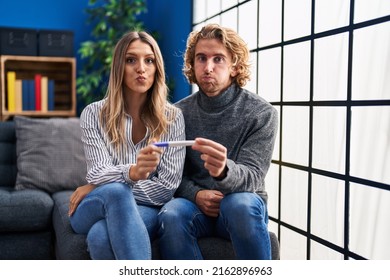 Young Couple Holding Pregnancy Test Result Puffing Cheeks With Funny Face. Mouth Inflated With Air, Catching Air. 