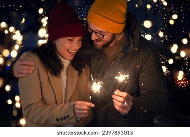 Young couple holding sparkler in the night - new year eve christmas holidays. Couple with firework outdoors enjoy emotion and feeling - Powered by Shutterstock