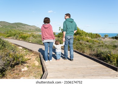 Young couple holding their little girl hands and walking on a wooden walkway at the mediterranean coast. Family holidays. First steps baby.   