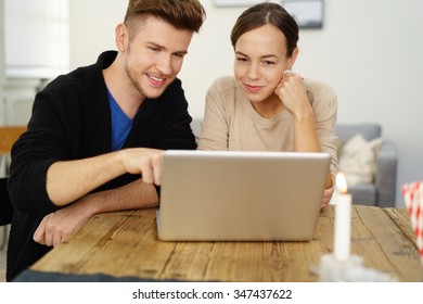 young couple at home focused on notebook with man pointing at screen