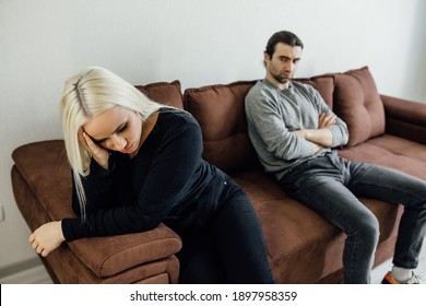 young couple at home. Handsome young man and attractive old woman are having relationship problems. Sitting on sofa together and looking to opposite sides.