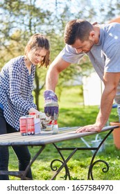 Young Couple As A Home Improvement Paints And Renovates Together A Table In The Garden In Summer