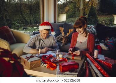 Young couple at home with their pet dog at Christmas time. They are writing out cards and wrapping presents together. - Powered by Shutterstock