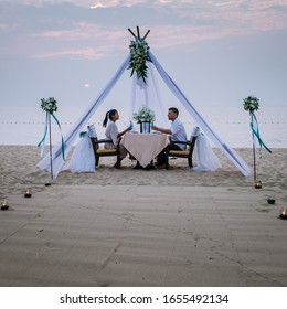 Young Couple Honeymoon Dinner By Candle Light During Sunset On The Beach, Men And Woman Having Dinner On The Beach Romantic Setting In Thailand During Sunset Pattaya