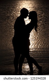 Young couple hug silhouette on a sea beach against sunset background
