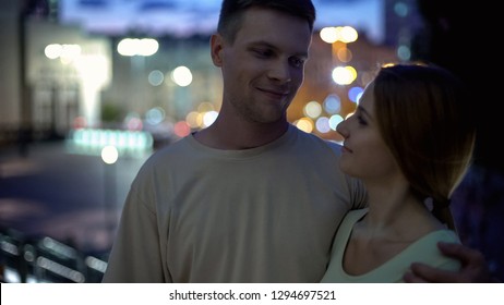 Young couple hugging against night city background, sense of reliability comfort