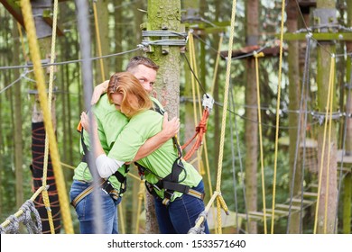 Young Couple Hugging Happily In The Climbing Forest Or High Ropes Course At The Climbing Course