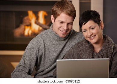 Young couple hugging on sofa at home in winter, using laptop computer, smiling. - Powered by Shutterstock