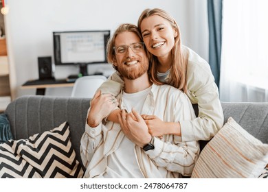 Young couple hugs on a sofa at home, smiling and happy, showing love and togetherness, looking at camera. Relationship concept - Powered by Shutterstock