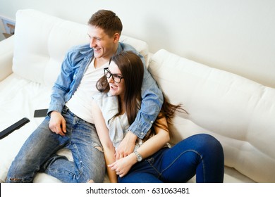 Junge Ehemann und Ehefrau, die auf Sofa sitzen und fernsehen und lächeln