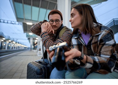 A young couple immersed in conversation while reviewing photos on a camera, enjoying a relaxed moment during their travels. - Powered by Shutterstock